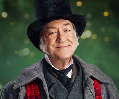 A smiling Scrooge with a caption that reads “holiday joy: past, present, future”