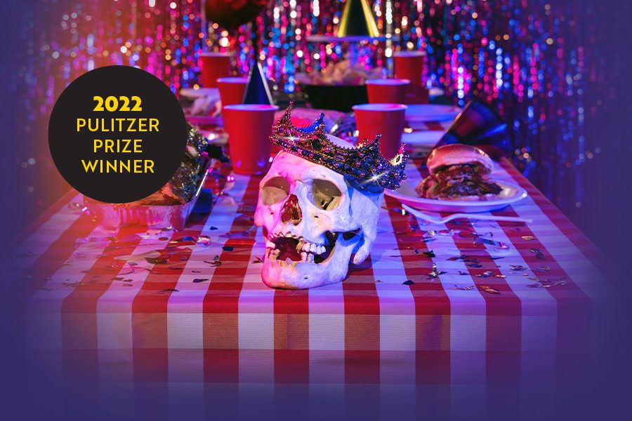 A jewel-encrusted crown adorns a skull sitting on a table littered with red Solo cups and barbecued meats.