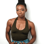 A black person with hair in a bun, an olive green halter tank top, and blue jeans.