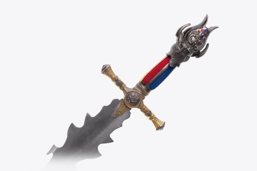 A jagged-tooth dagger with an elaboratively decorated hilt is topped with a stylized head featuring abundant facial hair.