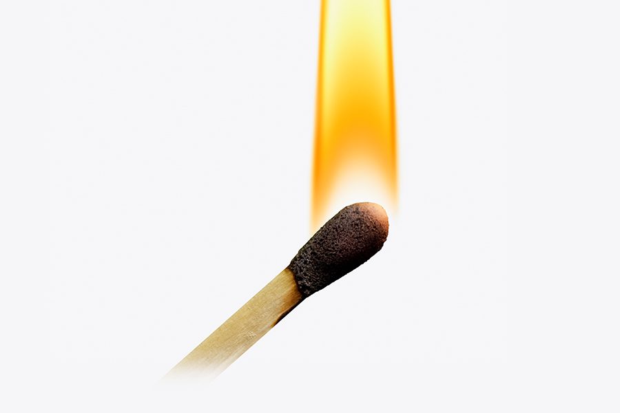 A golden yellow flame, outlined in orange, rises up from the head of a lit wooden match.